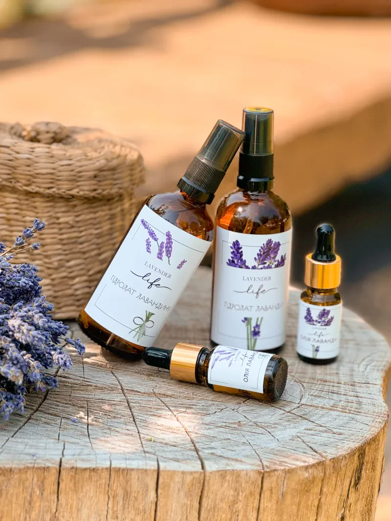 Флакони гідролату лаванди й лавандину та пляшечки ефірної олії Lavender Life на дерев'яному спилі поруч із сухою лавандою